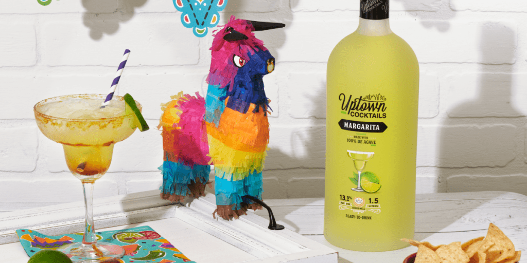 Pinata in between margarita in a glass and Uptown Cocktails Margarita bottle